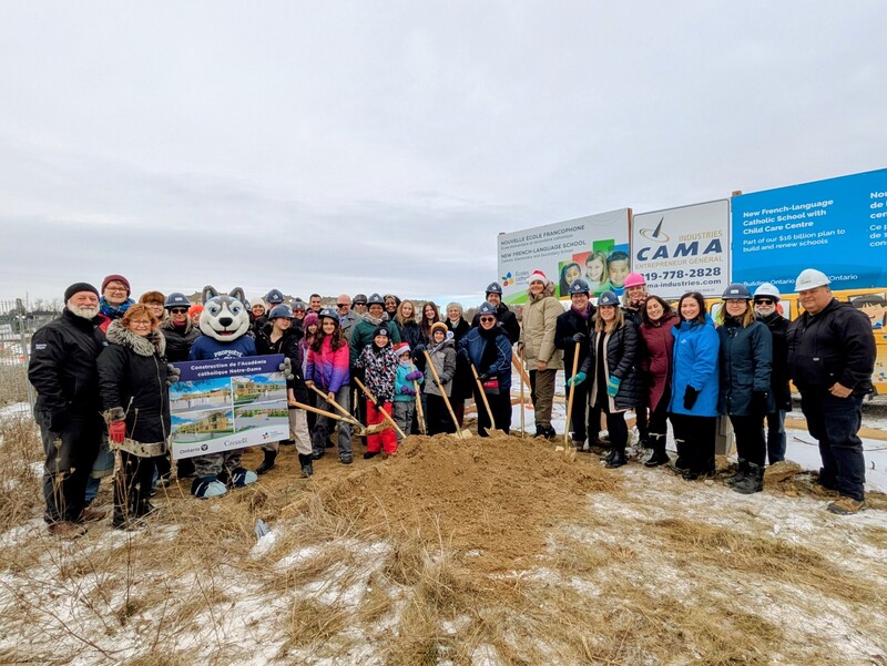 Membres de la communauté, représentants du CECCE et représentants politiques rassemblés à l'extérieur sur le terrain de construction pour une photo officielle de la pelletée de terre. 
