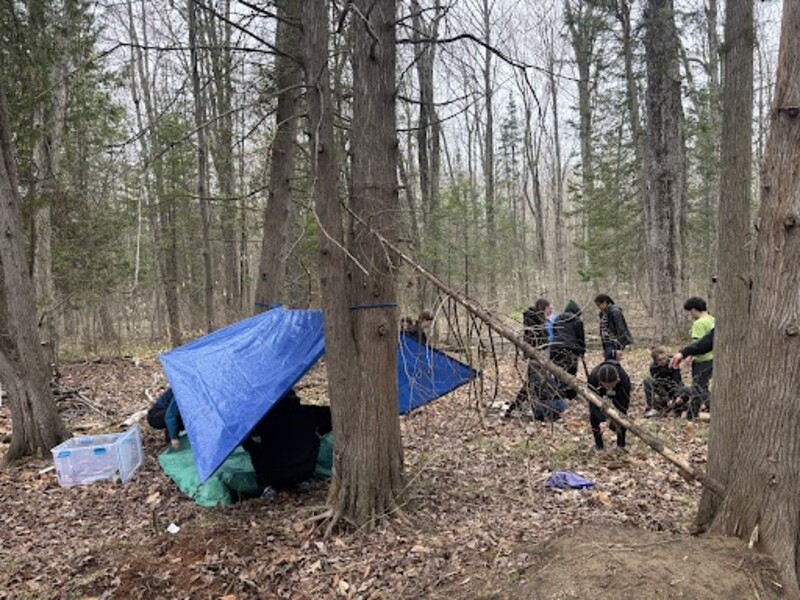 Élèves construisant un abri de survie en forêt.