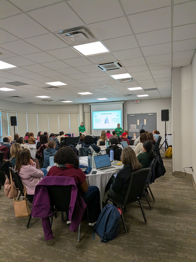 Deux animatrices présentent un atelier de formation devant des participantes réunies autour de tables, avec des ordinateurs portables et du matériel pédagogique.