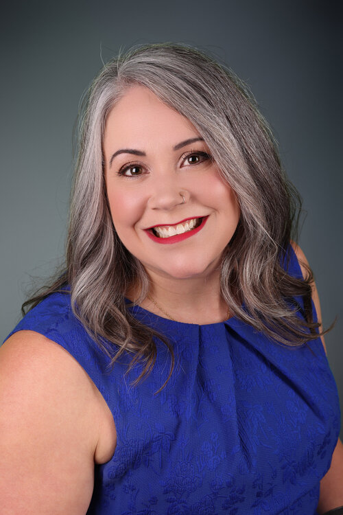 Portrait professionnel de Jolène Savoie-Day souriante, portant une robe bleu vif sans manches et arborant un piercing au nez.