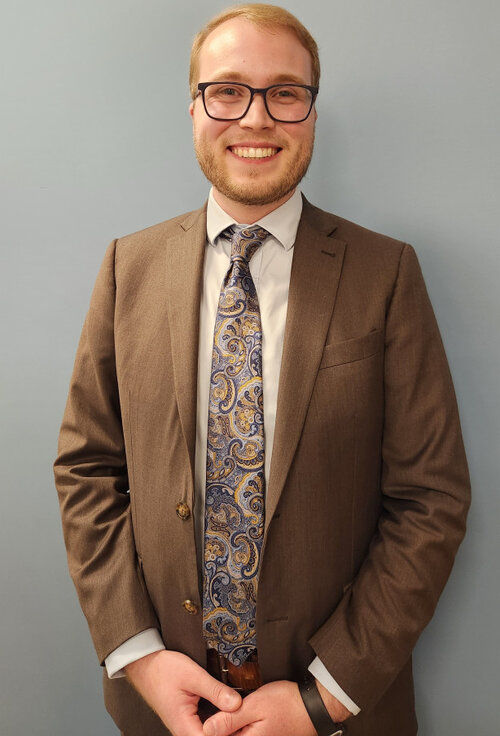 Portrait professionel de Olivier Tremblay-Venneri, vêtu d'un complet brun, une chemise pâle et une cravate à motifs bleus et dorés.