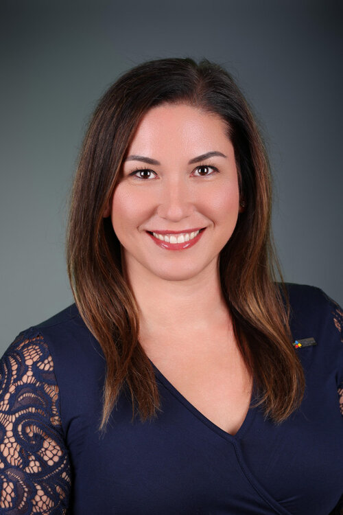 Karyne Chamberland souriante, vêtue d’un haut bleu marine à manches en dentelle, sur fond neutre.