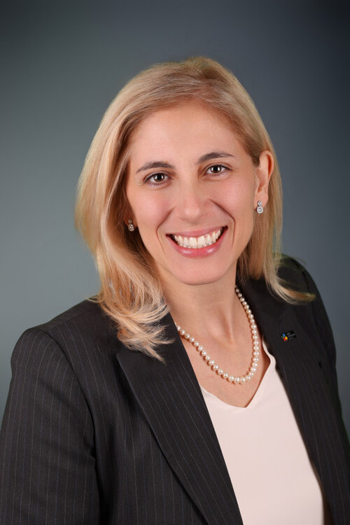 Valérie Intraligi, vêtue d’un veston rayé et d’un collier de perles, sur fond neutre.