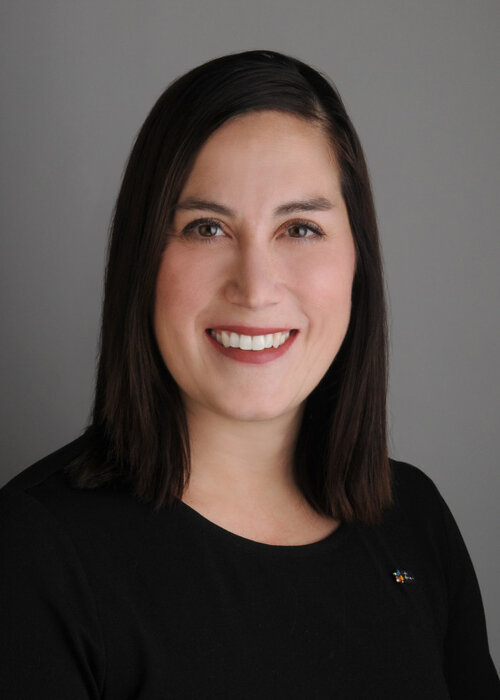 Valérie Samson souriante, vêtue de noir, les cheveux foncés au carré, sur fond gris neutre.