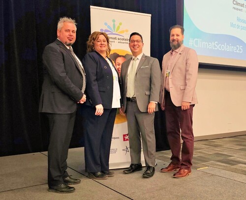 Quatre personnes posent devant une affiche du congrès sur le climat scolaire