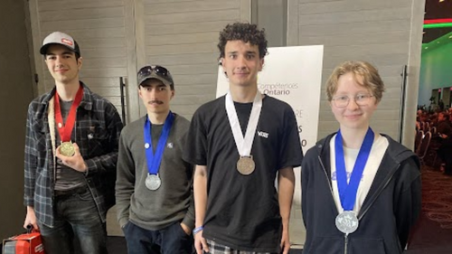 Jasmin Galand, Samuel Bissonnette, Brandon Foy et Eliot Lefrançois posent avec leurs médailles devant une affiche de Compétences Ontario