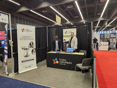 Deux personnes debout derrière une table d’exposition lors d’un salon professionnel.