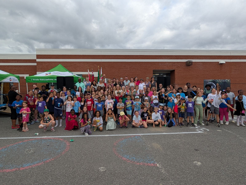 Grand groupe d’élèves et d’adultes rassemblés à l’extérieur devant une école lors d’un événement communautaire.