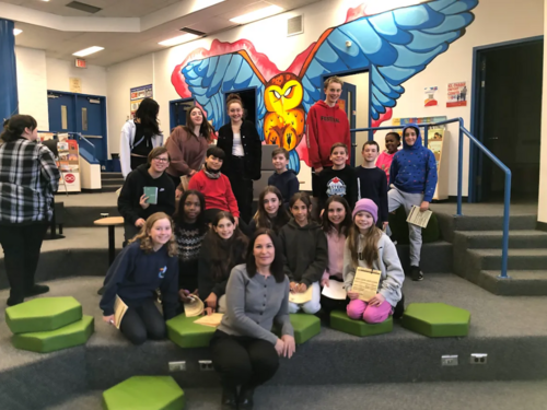 Groupe d’élèves posant avec une adulte dans une salle décorée d’une grande murale représentant un hibou coloré aux ailes déployées.