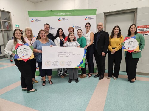 Groupe de membres du personnel scolaire posant devant une bannière des Écoles catholiques du Centre-Est, tenant des affiches portant le message « École communautaire citoyenne » et « Un réseau d’écoles engagées pour une société transformée »