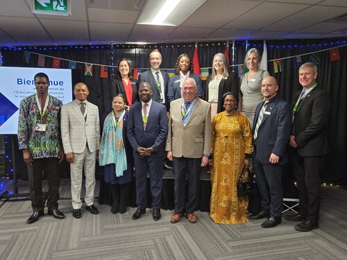Groupe de personnes posant ensemble devant une scène décorée de drapeaux de différents pays lors d’un événement officiel.