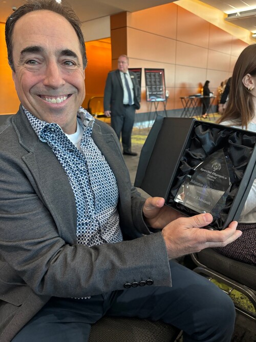 Pierre Thériault tient son trophée d’Éducateur de l’année des Olympiques spéciaux Ontario – Ottawa et sourit à l’objectif.