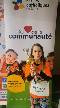 Noémie Anciaux tient son trophée devant une bannière des Écoles catholiques du Centre-Est lors d’un événement.