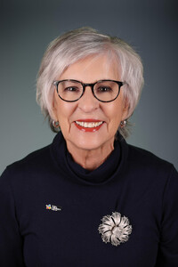 Portrait professionnel de Diane Burns souriante, portant un haut foncé avec broche florale argentée et lunettes noires.