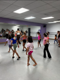 Groupe d’élèves dans un studio de danse suivant les instructions d’une enseignante devant un miroir mural.
