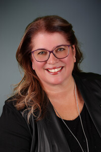 Portrait professionnel de Johanne Lacombe souriante, portant des lunettes mauves, un haut noir et un collier argenté.