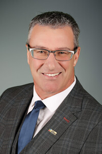 Portrait professionnel de Daniel Levasseur souriant, vêtu d’un complet à carreaux gris et d’une cravate bleue.