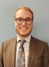 Portrait professionel de Olivier Tremblay-Venneri, vêtu d'un complet brun, une chemise pâle et une cravate à motifs bleus et dorés.