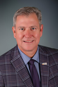 Portrait professionnel de Robert Rainboth souriant, vêtu d’un veston à carreaux mauves, d’une chemise bleue et d’une cravate violette.