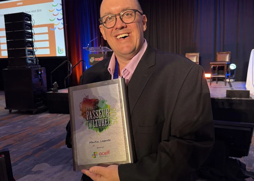 Martin Laporte tenant une plaque « Prix Passeur culturel 2025 » lors d’un événement sur scène.