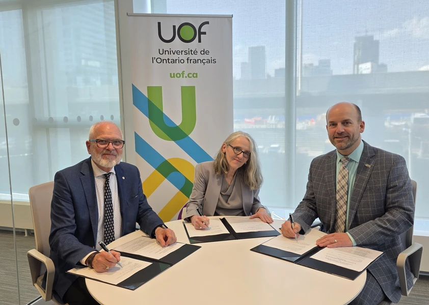 Marc Bertrand, directeur de l’éducation du CECCE, Normand Labrie, recteur et vice-chancelier de l’UOF, et Isabelle Dostaler, vice-rectrice aux études et à la recherche de l’UOF, sont assis autour d’une table et signent des documents officiels, devant une bannière de l’Université de l’Ontario français (UOF), dans un espace lumineux avec vue urbaine.