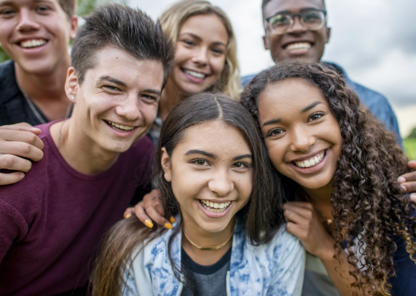 Groupe de cinq adolescents souriants réunis à l’extérieur.