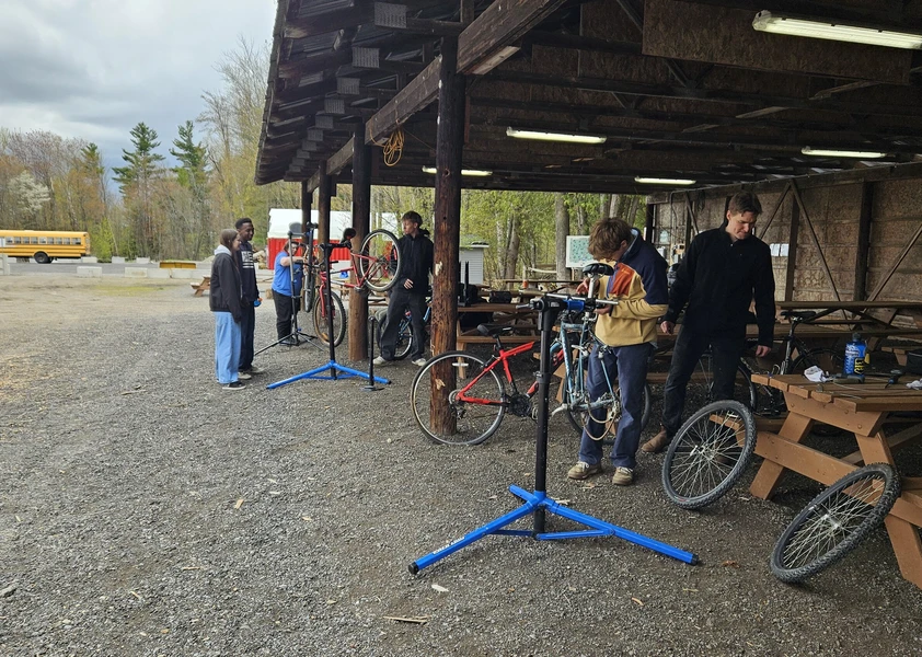 Des élèves réparent et entretiennent des vélos sous un abri extérieur lors d’un atelier de mécanique au Centre agro-éducatif du CECCE.