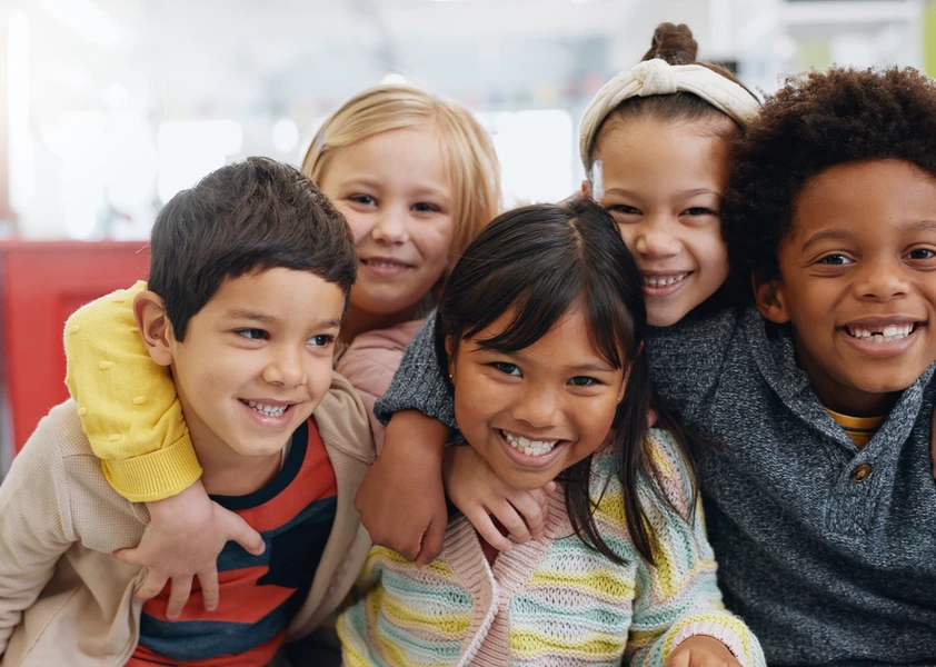 Cinq enfants souriants se tiennent dans les bras les uns des autres.