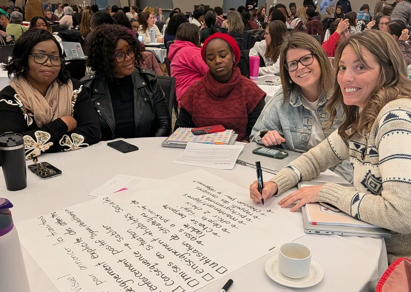 Cinq participantes échangent autour d’une table et prennent des notes sur de grandes feuilles lors d’un atelier de groupe.