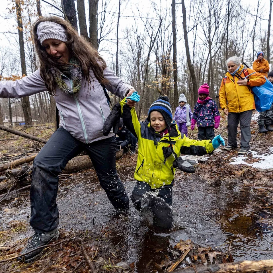 Groupe d’élèves traversant un ruisseau en forêt, guidés par des adultes, lors d’une sortie en plein air.