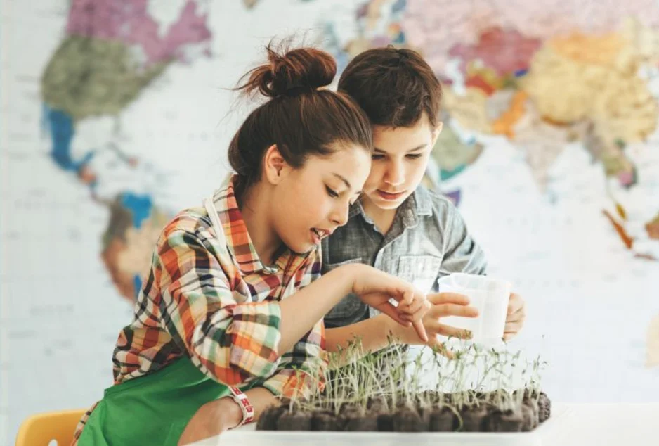 Deux élèves observent des pousses de plantes en classe, avec une carte du monde en arrière-plan.
