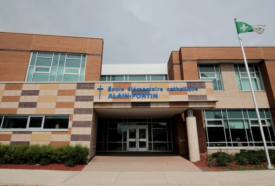 Façade de l’École élémentaire catholique Alain-Fortin, bâtiment moderne en briques aux teintes variées avec de grandes fenêtres. Le nom de l’école est affiché en bleu au-dessus de l’entrée. Un drapeau franco-ontarien flotte à droite.