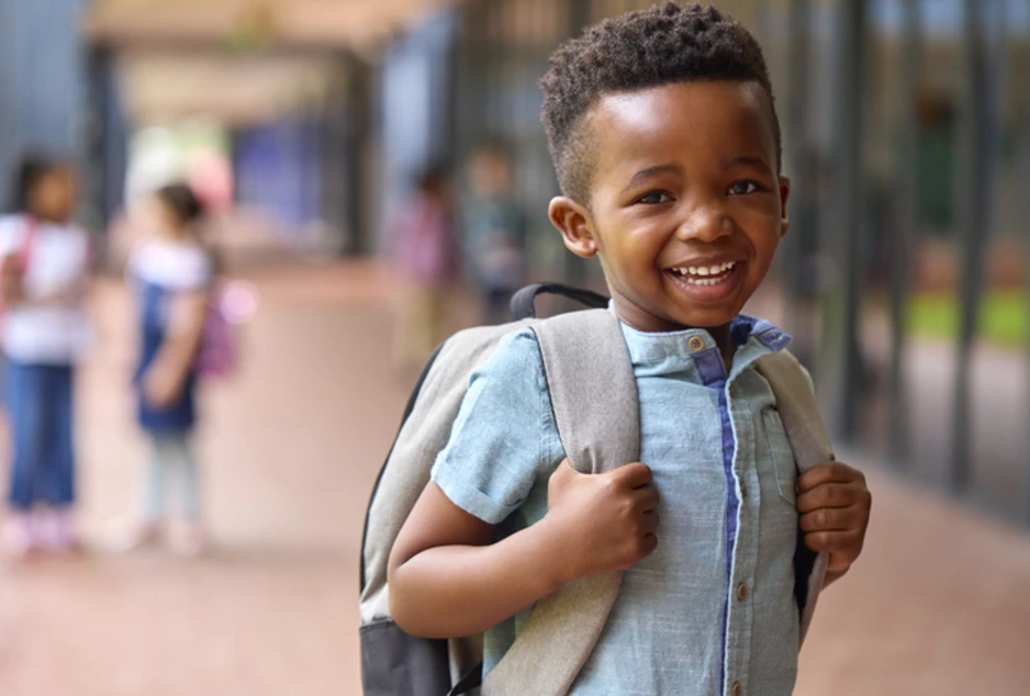 Portrait d'un élève souriant d'école primaire, sac à dos à l'extérieur, à l'école