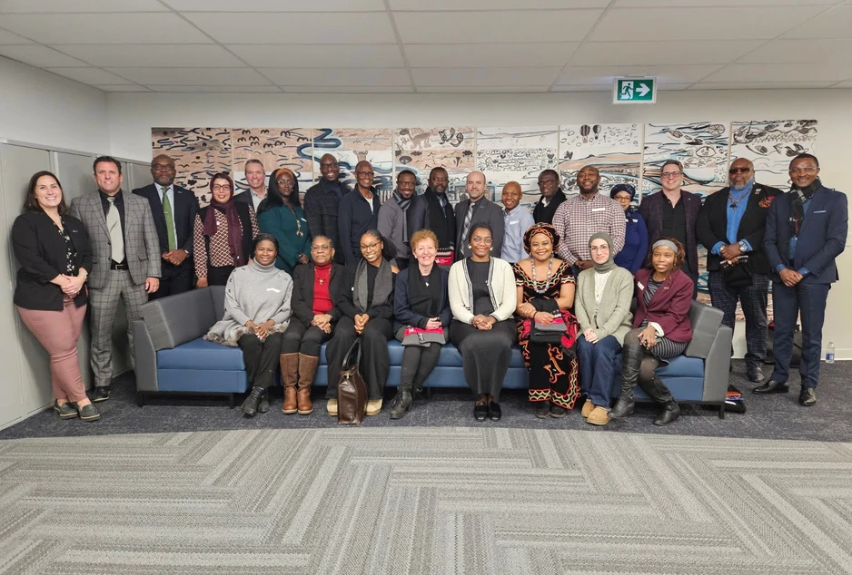 Photo de groupe d’une vingtaine d’adultes issus de la diversité, certains assis sur un divan et d’autres debout derrière, réunis à l’intérieur et souriant face à la caméra.