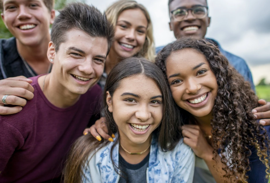Groupe de cinq adolescents souriants réunis à l’extérieur.
