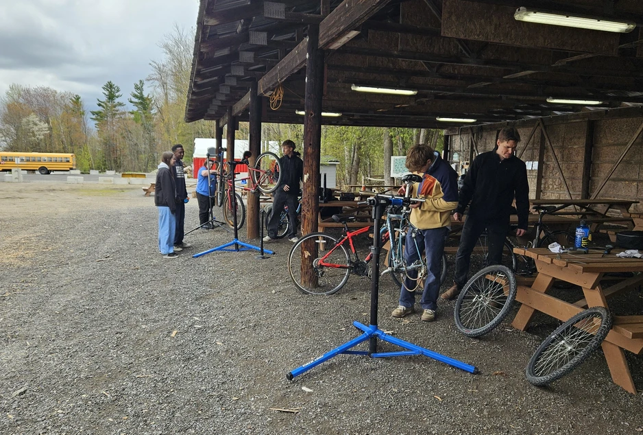 Des élèves réparent et entretiennent des vélos sous un abri extérieur lors d’un atelier de mécanique au Centre agro-éducatif du CECCE.