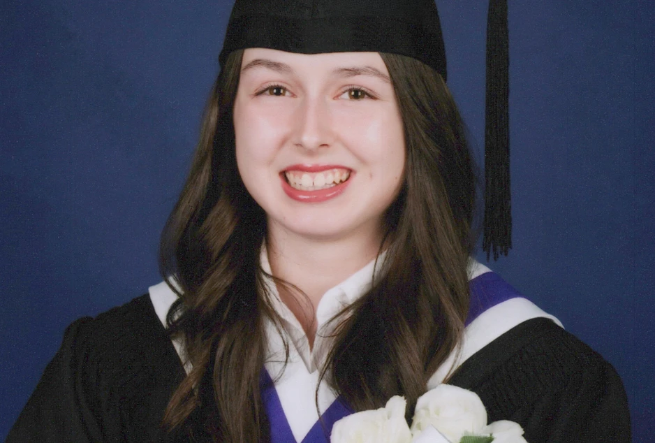 Portrait officiel de fin d’études de Kaylee Gagné portant une toge noire et un mortier de diplômée. Elle tient un bouquet de roses blanches accompagné d’un rouleau de diplôme marqué « 2025-2026 » devant un fond bleu uni et sourit à la caméra.