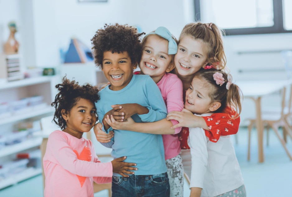 Cinq jeunes enfants souriants se font un câlin dans une salle de classe.