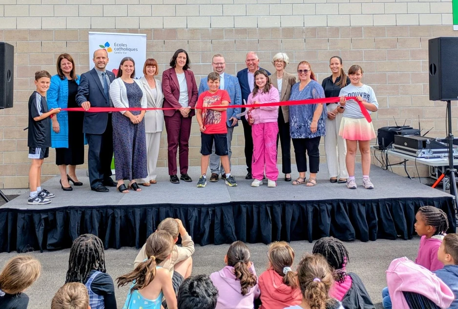 Des dignitaires, des membres du Conseil, la direction de l’école et des élèves procèdent à la coupure du ruban lors de l’inauguration officielle de l’École élémentaire catholique Marie-Soleil, sous le regard des élèves rassemblés devant la scène.