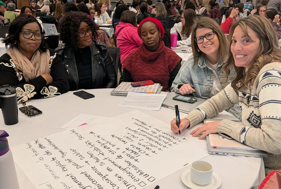 Cinq participantes échangent autour d’une table et prennent des notes sur de grandes feuilles lors d’un atelier de groupe.