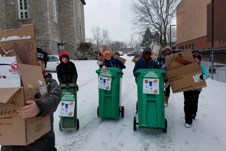 Des élèves transportent des bacs de compostage et des boîtes de carton dehors, en hiver, à l’école.