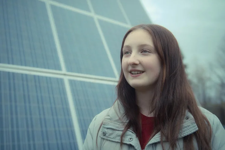 Élève souriante devant de grands panneaux solaires extérieurs