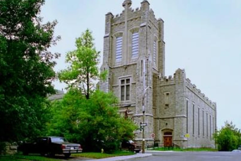 Photographie de l’église de l’École secondaire catholique Saint-Jean-Baptiste à Ottawa, un édifice patrimonial en pierre avec une tour centrale, entouré d’arbres et situé à un coin de rue.