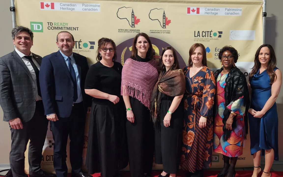 Huit adultes posent sur un tapis rouge devant une bannière de partenaires, lors de la remise du Prix du partenaire distingué au CECCE par l’Association des Africains Canadiens d’Ottawa.