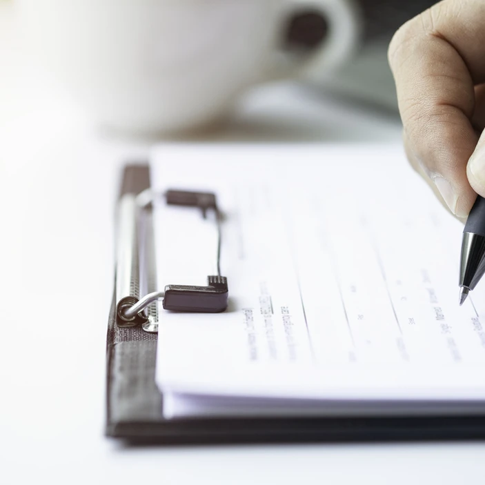 Main tenant un stylo et remplissant un formulaire sur une planchette à pince