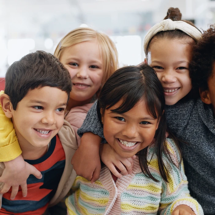Cinq enfants souriants se tiennent dans les bras les uns des autres.
